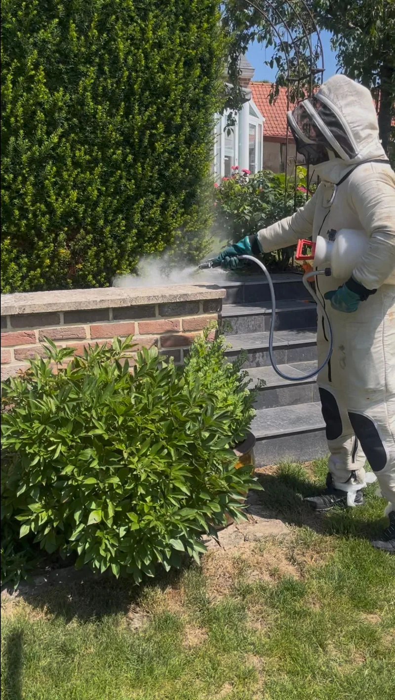 Technicien en combinaison effectuant une pulvérisation insecticide en extérieur
